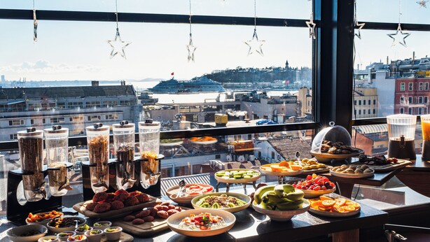 A buffet table with various food items and a view of a cityscape through a window. - SuB Karaköy - Special Class (Istanbul)