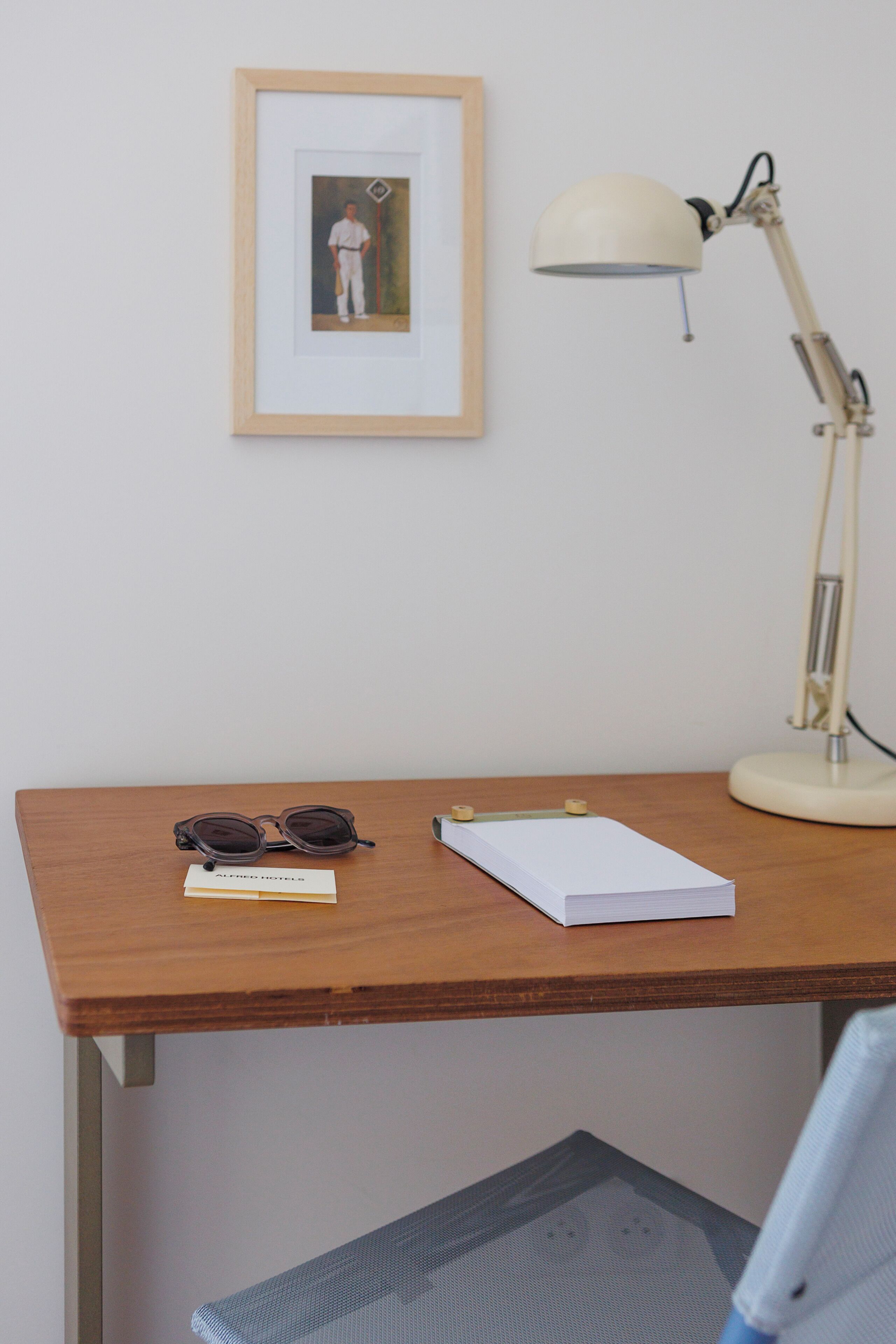 A wooden desk with a framed picture, a desk lamp, a pair of sunglasses, and a notebook.