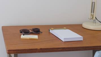 A wooden desk with a framed picture, a desk lamp, a pair of sunglasses, and a notebook.