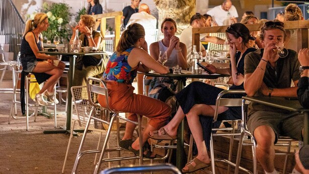 Een terras met tafels en stoelen onder parasols, omringd door bomen.