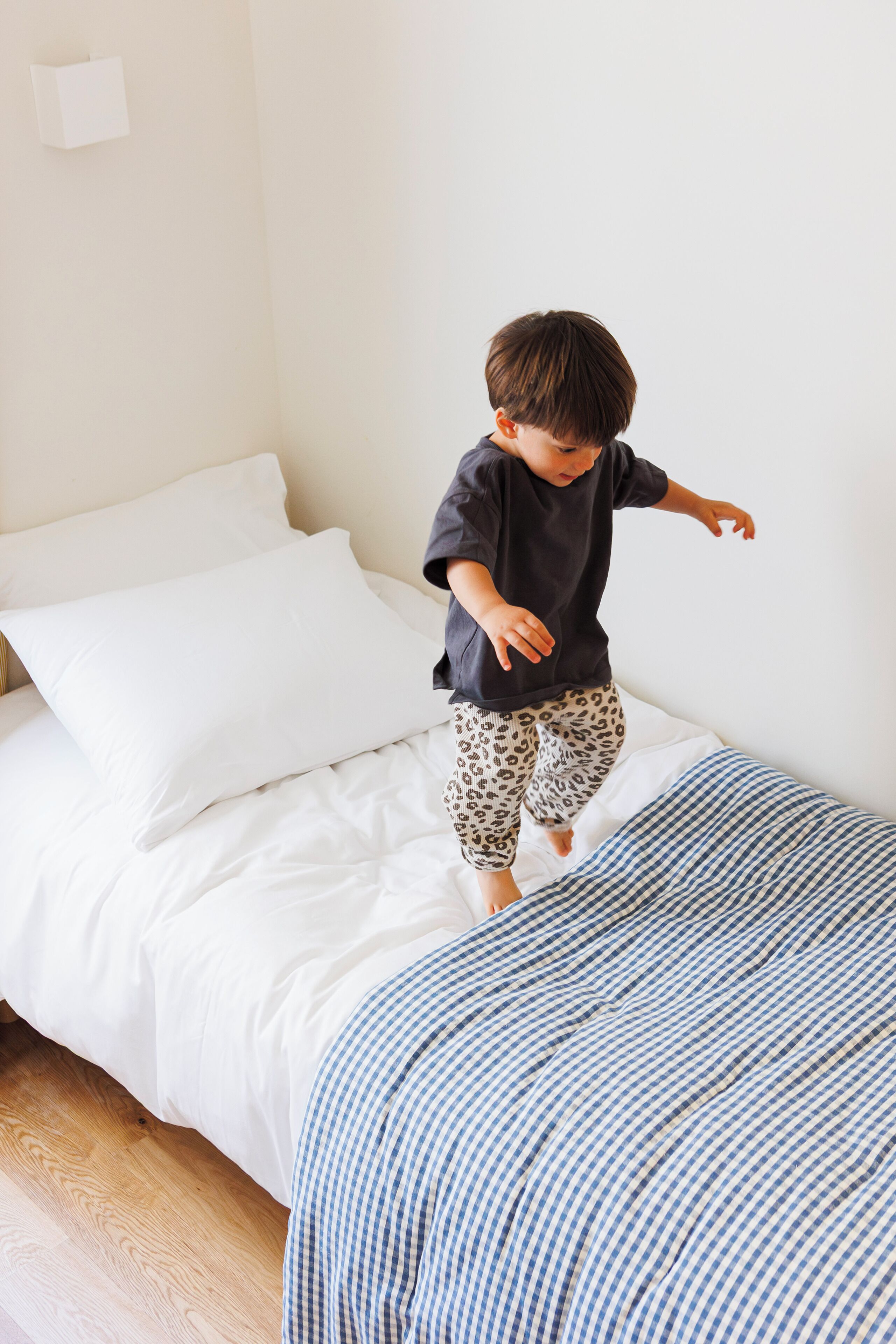 A child jumping on a bed with white and blue striped bedding.