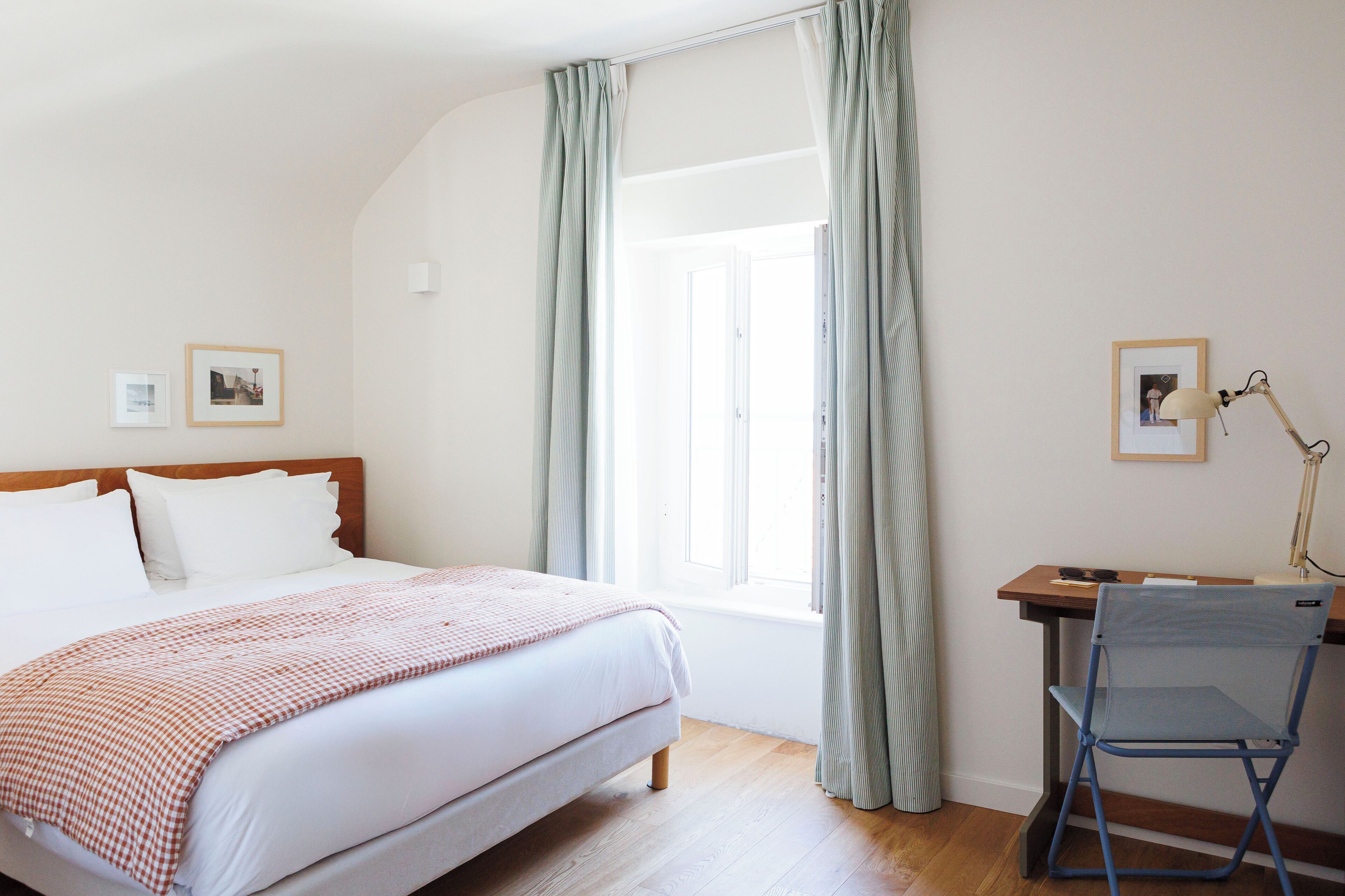 A bedroom with a bed, a desk, a chair, and a window with curtains.