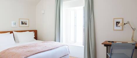 A bedroom with a bed, a desk, a chair, and a window with curtains.