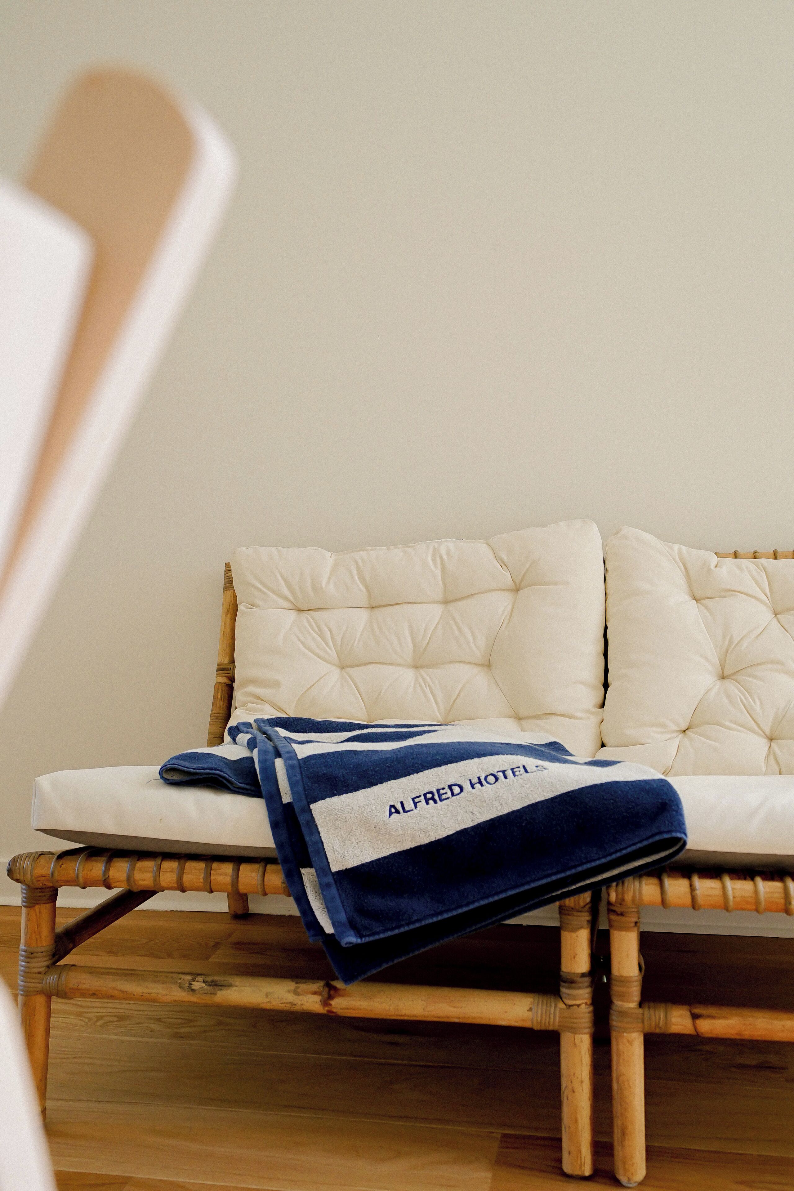 Un lit avec une tête de lit blanche et une couverture bleue sur laquelle on peut lire le texte « ALFRED HOTEL ».