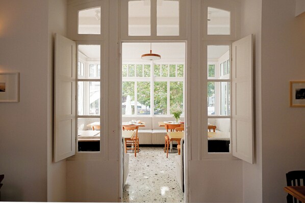 A hallway leading to a dining area with a bench and tables, large windows, and a ceiling light.