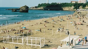 Een strand met parasols, mensen en een vuurtoren in de verte.