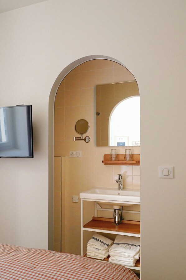 Un baño con televisión montada en la pared, un lavabo con espejo arriba y un perchero con toallas dobladas.