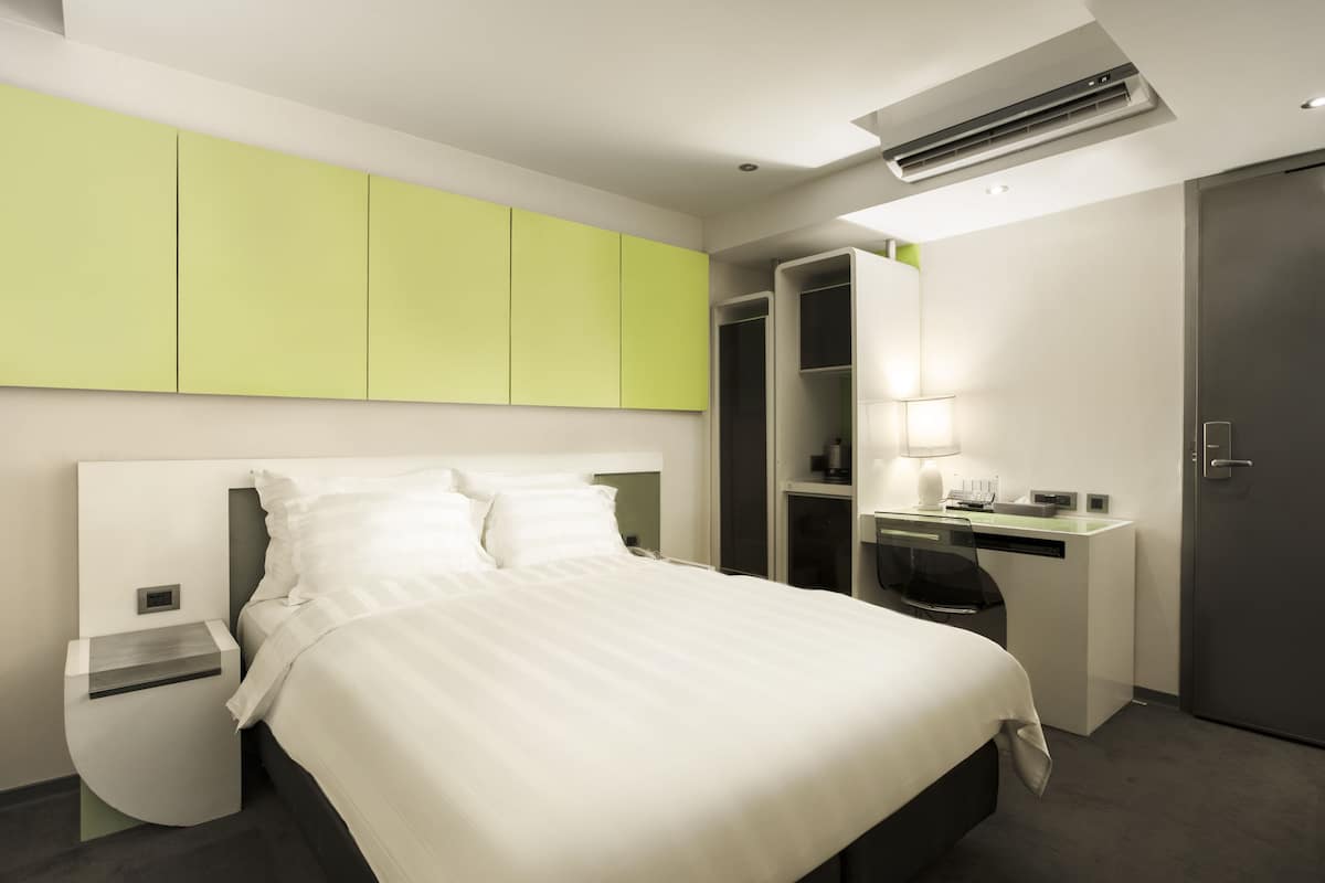 A modern hotel room with a bed, a desk, and a wardrobe.