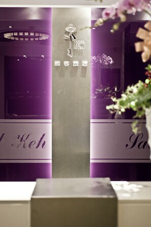 Un letrero de hotel con un logotipo y el nombre del establecimiento, un mostrador de recepción y una pared morada.