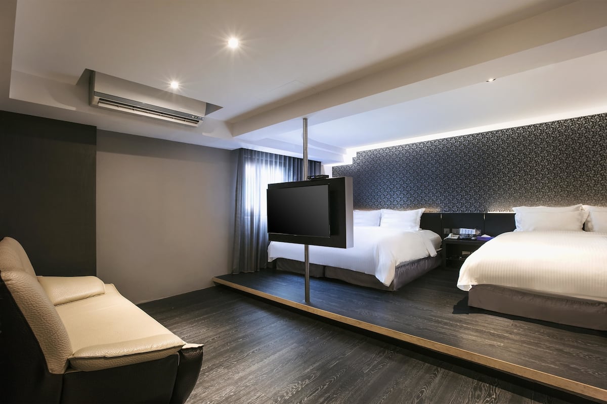 A modern hotel room with a large bed, a smaller bed, a flat-screen TV, a sofa, and a patterned wall.