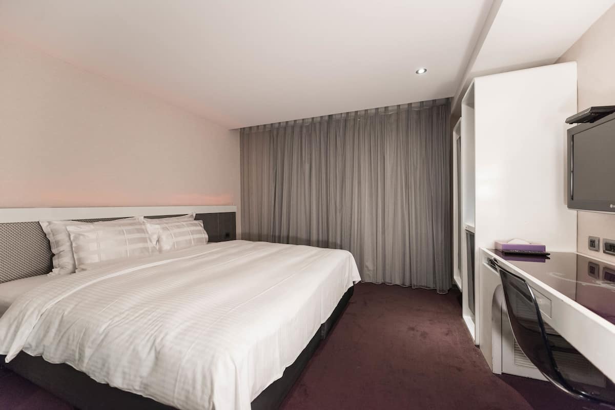 A hotel room with a bed, a desk, a television, and a window with curtains.