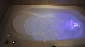 Een badkuip met een whirlpoolfunctie en twee verlichte knoppen.