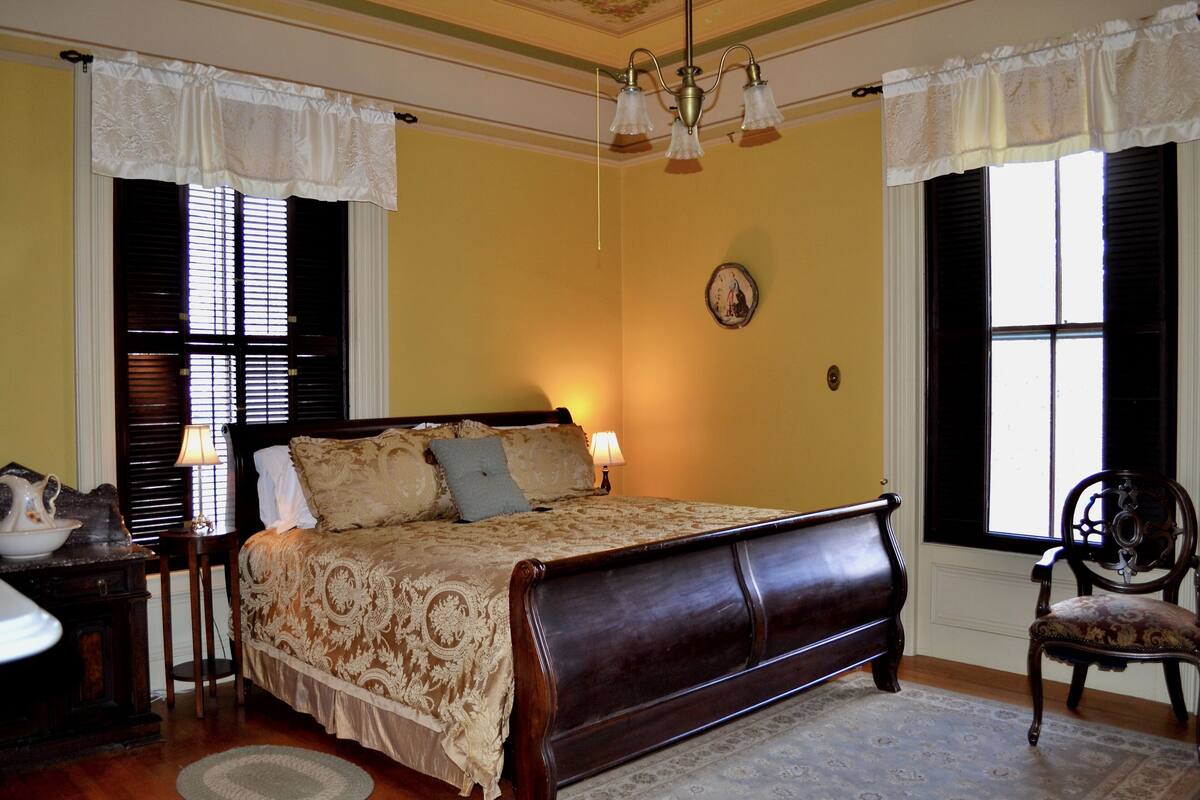 A bedroom with a large bed, a chair, a nightstand, and a lamp.