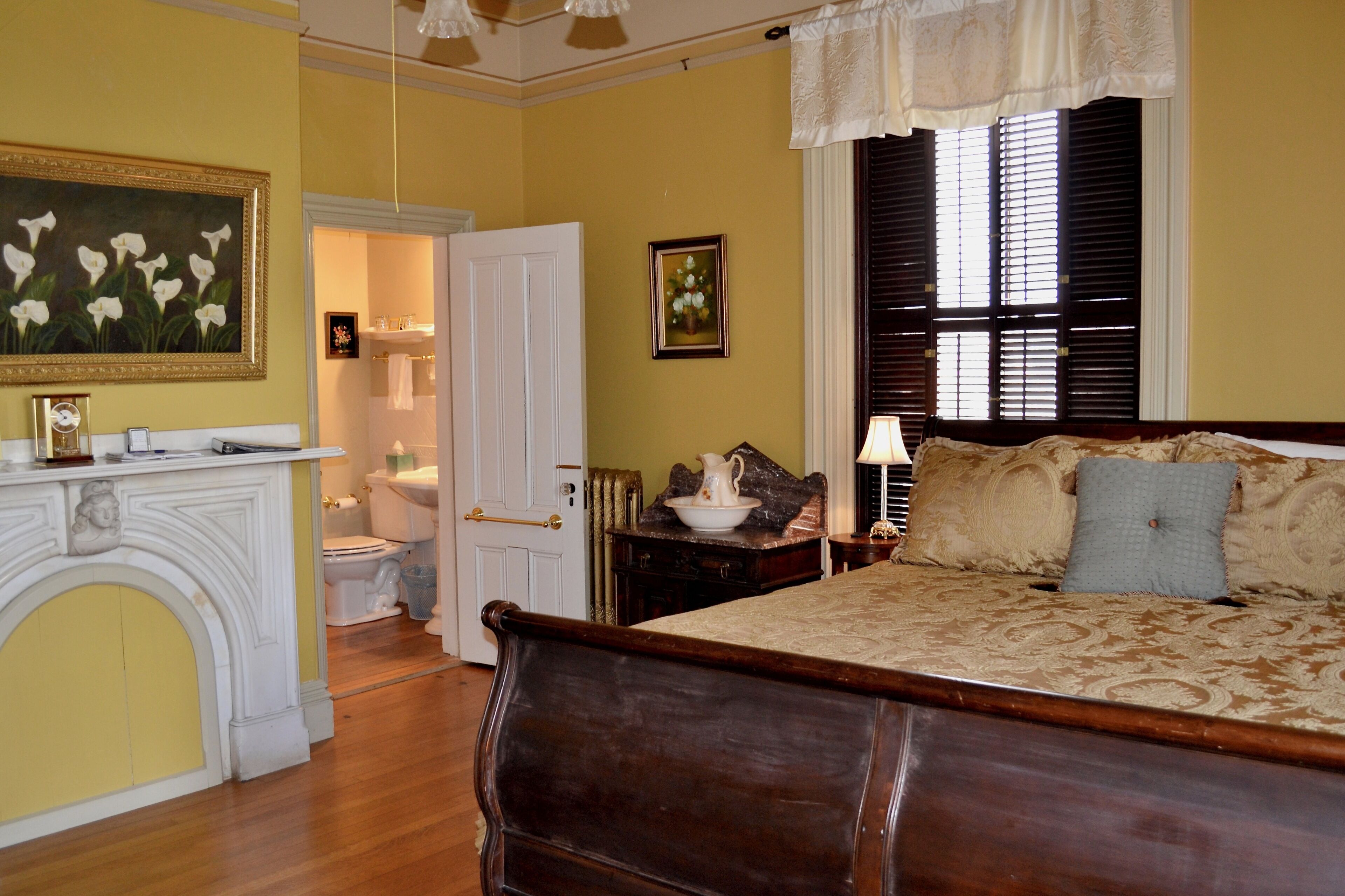 A bedroom with a bed, a nightstand, a dresser, a fireplace, and a bathroom visible through an open door.
