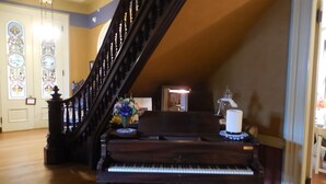 Ein Flügel in einem geräumigen Zimmer mit einer Holztreppe und Buntglasfenstern.