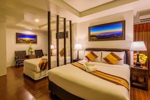 Quarto de hotel com duas camas, uma pintura grande, uma cadeira e uma mesa de cabeceira com abajur.