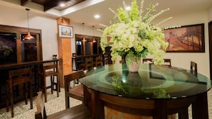 Un coin repas avec une table ronde en verre, des chaises en bois et un arrangement floral en guise de décoration centrale.