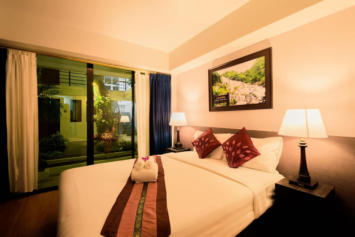 A hotel room with a large bed, two bedside lamps, a framed picture on the wall, and a view of a garden through the window.