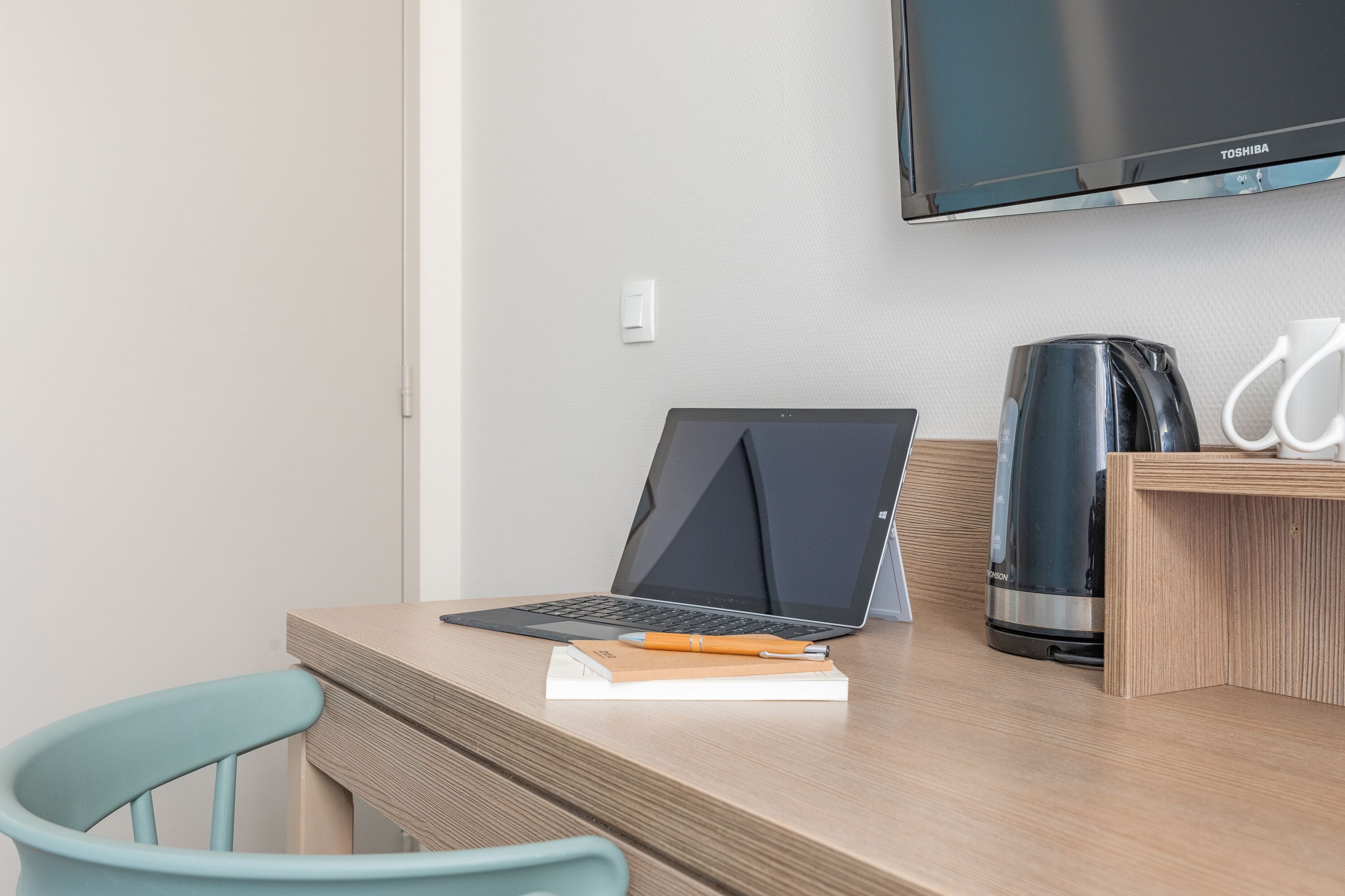 Um espaço de trabalho moderno com um laptop, um caderno, uma caneta, uma máquina de café e uma cadeira.