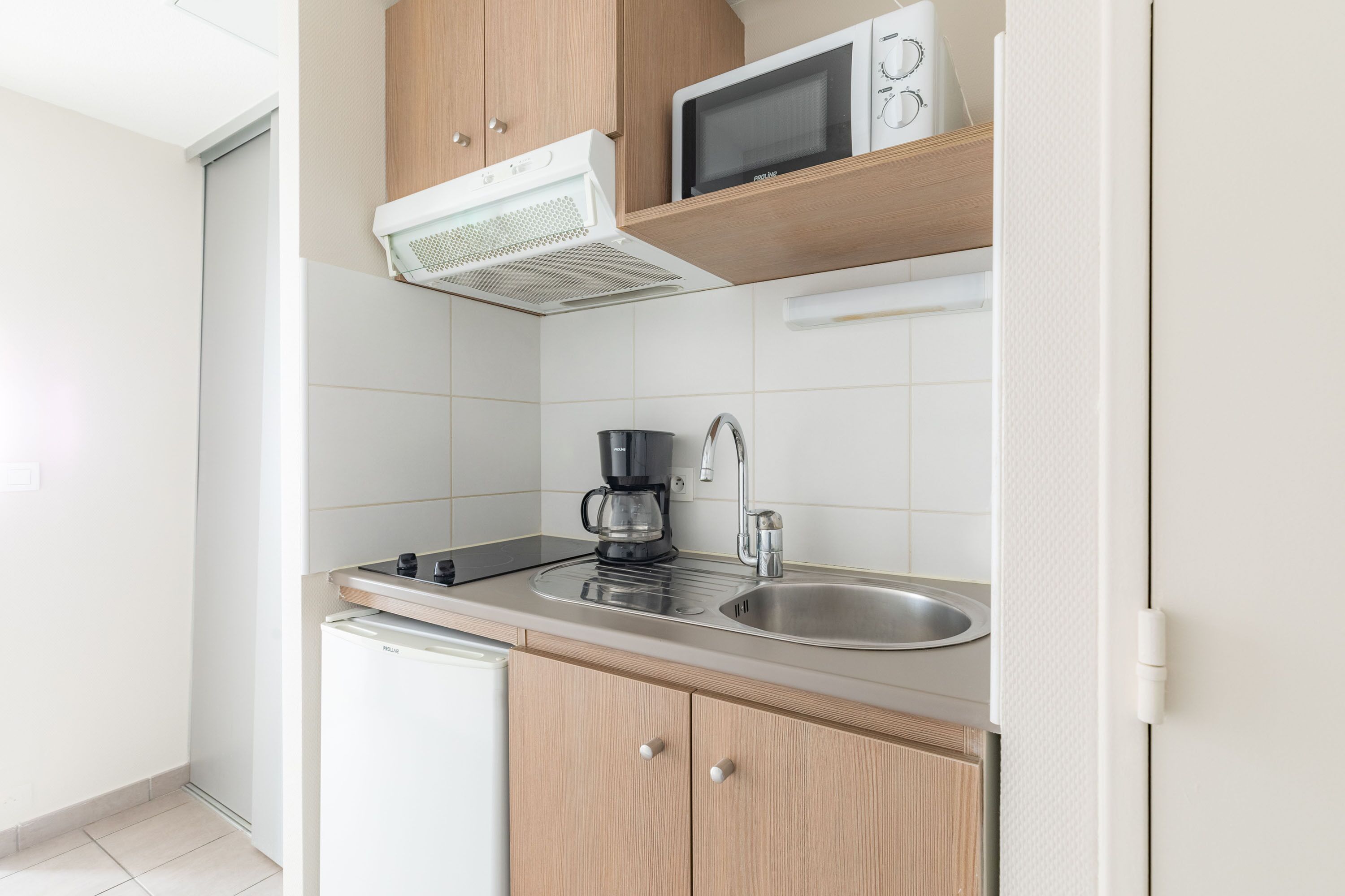 Cocina pequeña equipada con microondas, cafetera y lavamanos.