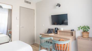 A hotel room with a bed, a desk with a laptop, a TV, and a plant.