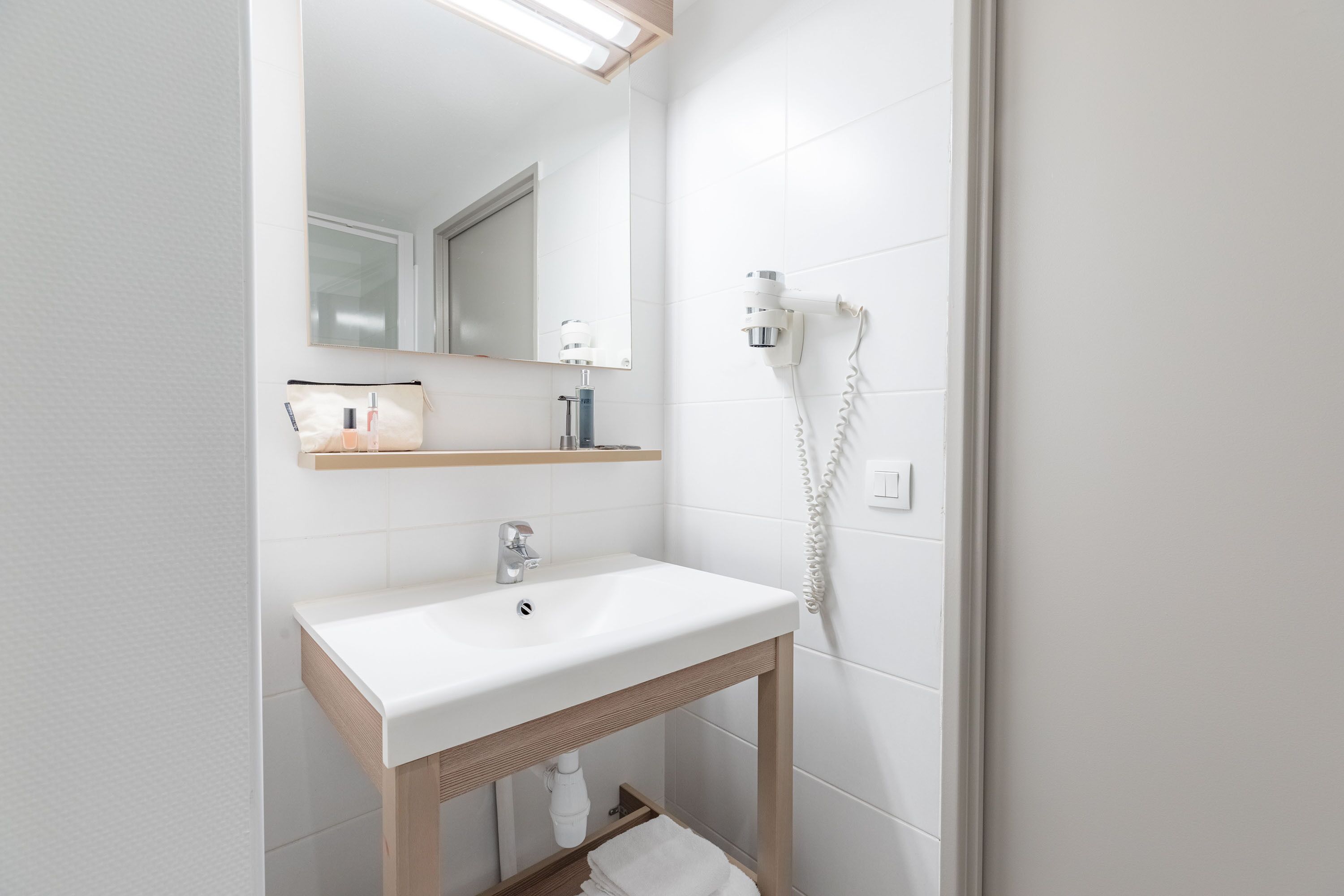 Une salle de bain moderne avec un lavabo blanc, un meuble-lavabo en bois et un miroir au-dessus.