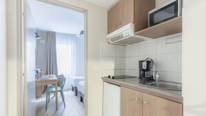 A compact kitchen with a microwave, coffee maker, and a small refrigerator. There is a dining area with a table and chairs visible through an open door. - Appart'City Classic Valence (Valence)