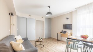 A modern living room with a grey sofa, a small round table with a plant, and a dining area with a wooden table and chairs. - Appart'City Classic Valence (Valence)
