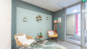A reception area with two wicker chairs, a small table with a plant, and a wall-mounted shelf with decorative items. - Appart'City Classic Valence (Valence)