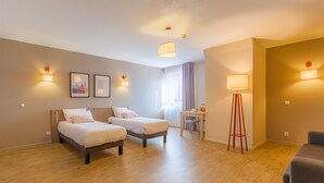 Een hotelkamer met twee bedden, een bureau, een stoel en een vloerlamp.