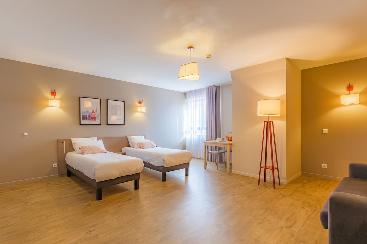 Une chambre d’hôtel avec deux lits, un bureau, une chaise et une lampe sur pied.