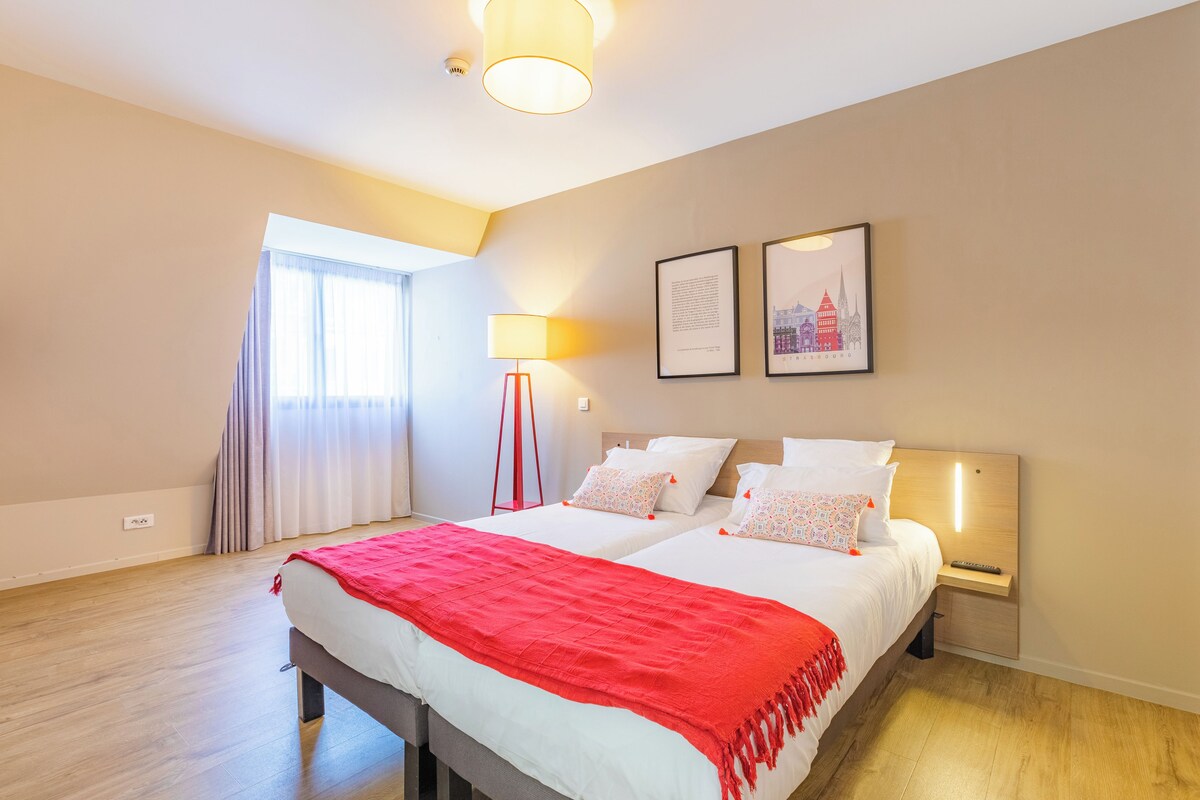 A hotel room with a large bed, two bedside tables, a lamp, and two framed pictures on the wall.