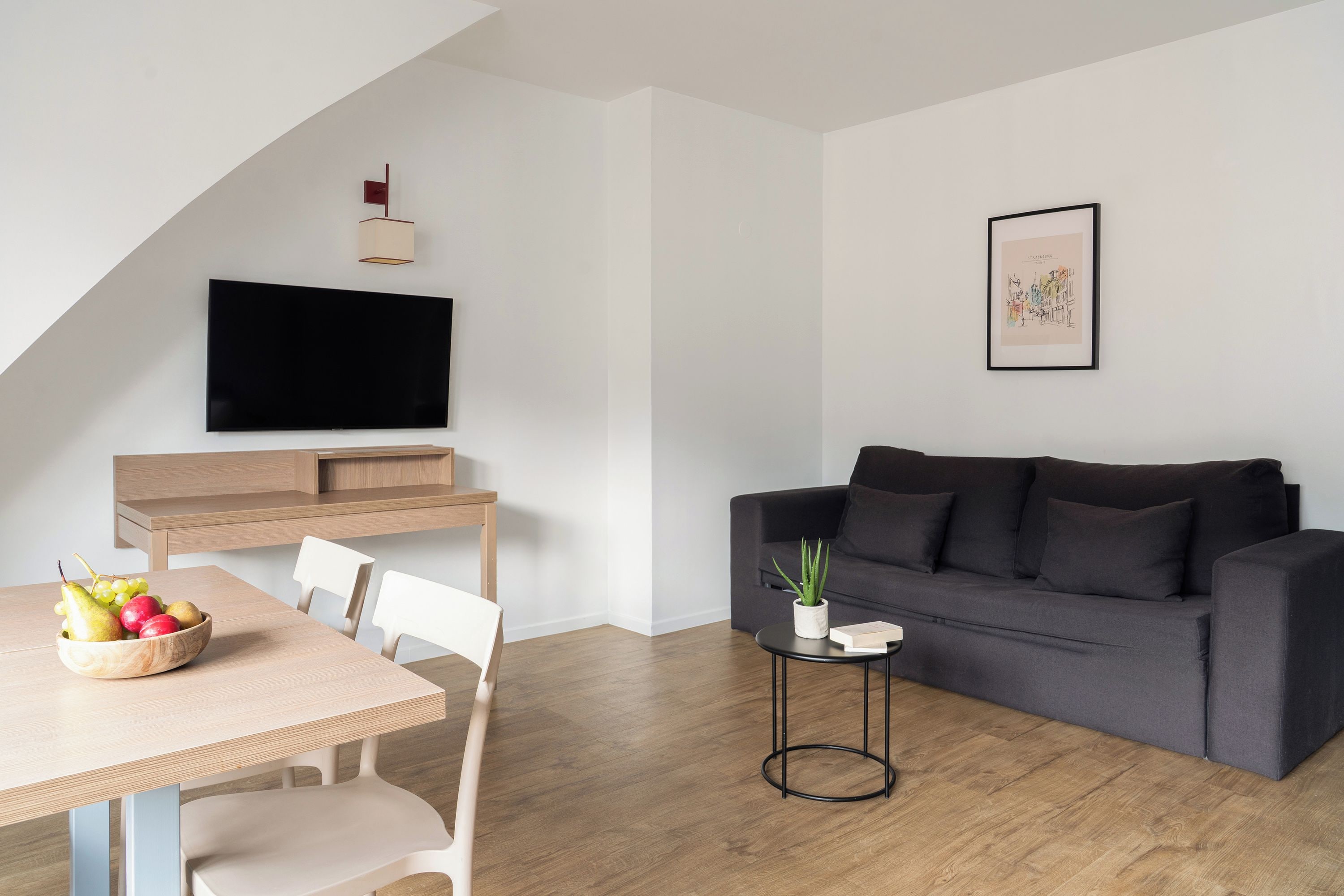 Un salon moderne doté d’un téléviseur à écran plat, d’un canapé gris foncé et d’un coin repas avec une table et des chaises en bois.