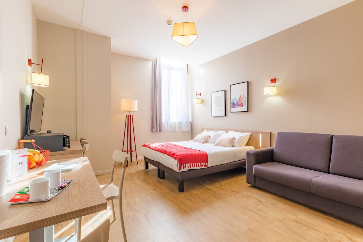 Une chambre d’hôtel moderne équipée d’un lit, d’un canapé, d’un bureau avec un ordinateur et d’une fenêtre avec des rideaux.