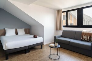 Un dormitorio moderno con cama, sofá, una mesita y una ventana con cortinas.