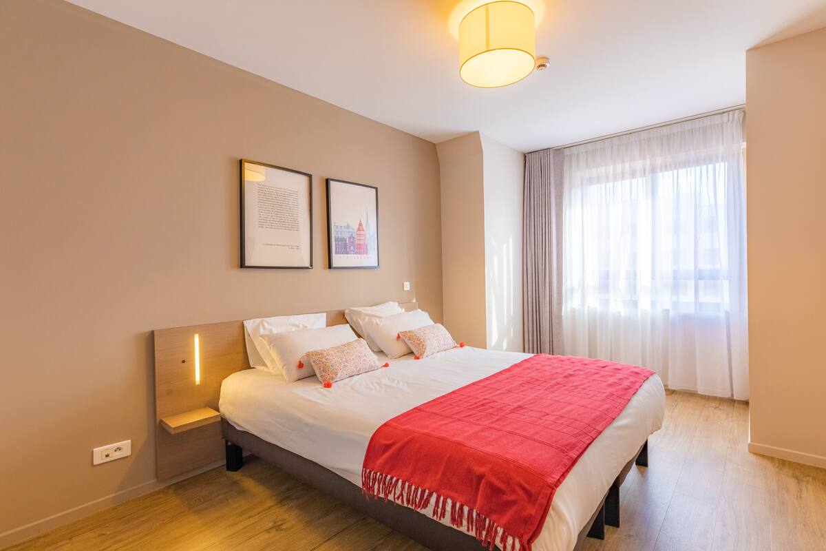 Une chambre à coucher bien rangée, avec un lit, des tables de chevet et une fenêtre avec des rideaux.