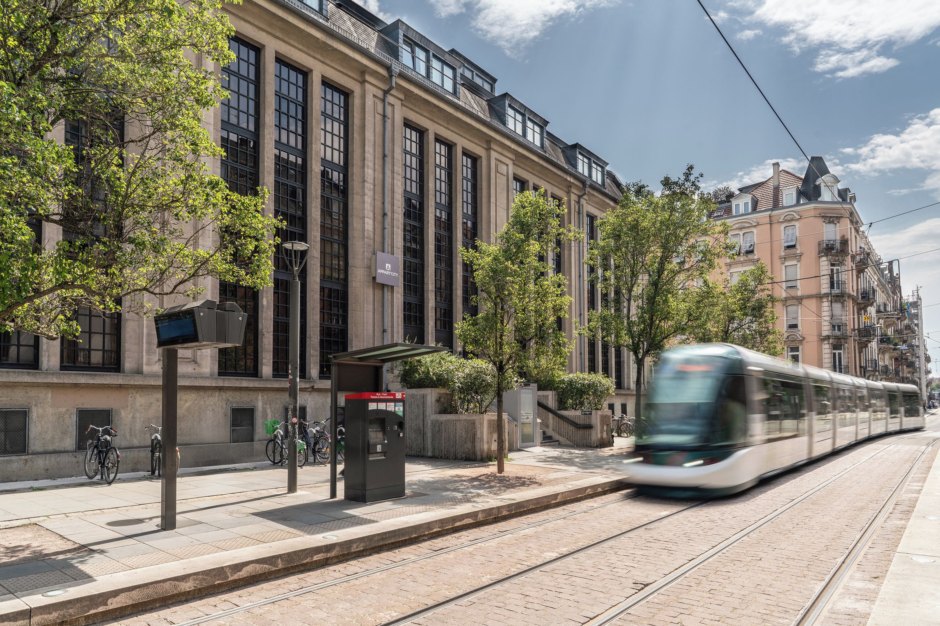 Een tram rijdt langs een gebouw met grote ramen en een overdekte wachtruimte.