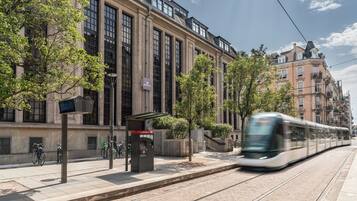 Een tram rijdt langs een gebouw met grote ramen en een overdekte wachtruimte.