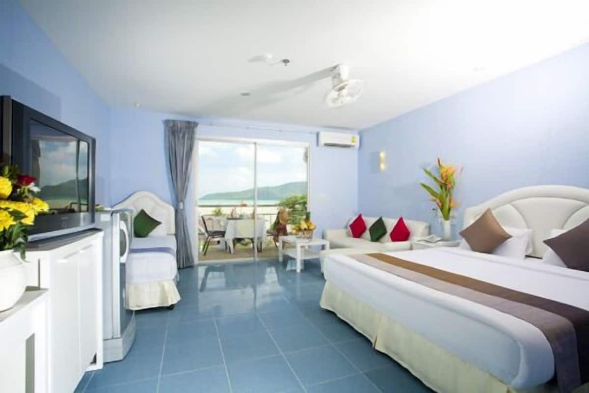 Une chambre d’hôtel avec un lit, une télévision, un balcon avec une table et des chaises, et une vue sur la mer.