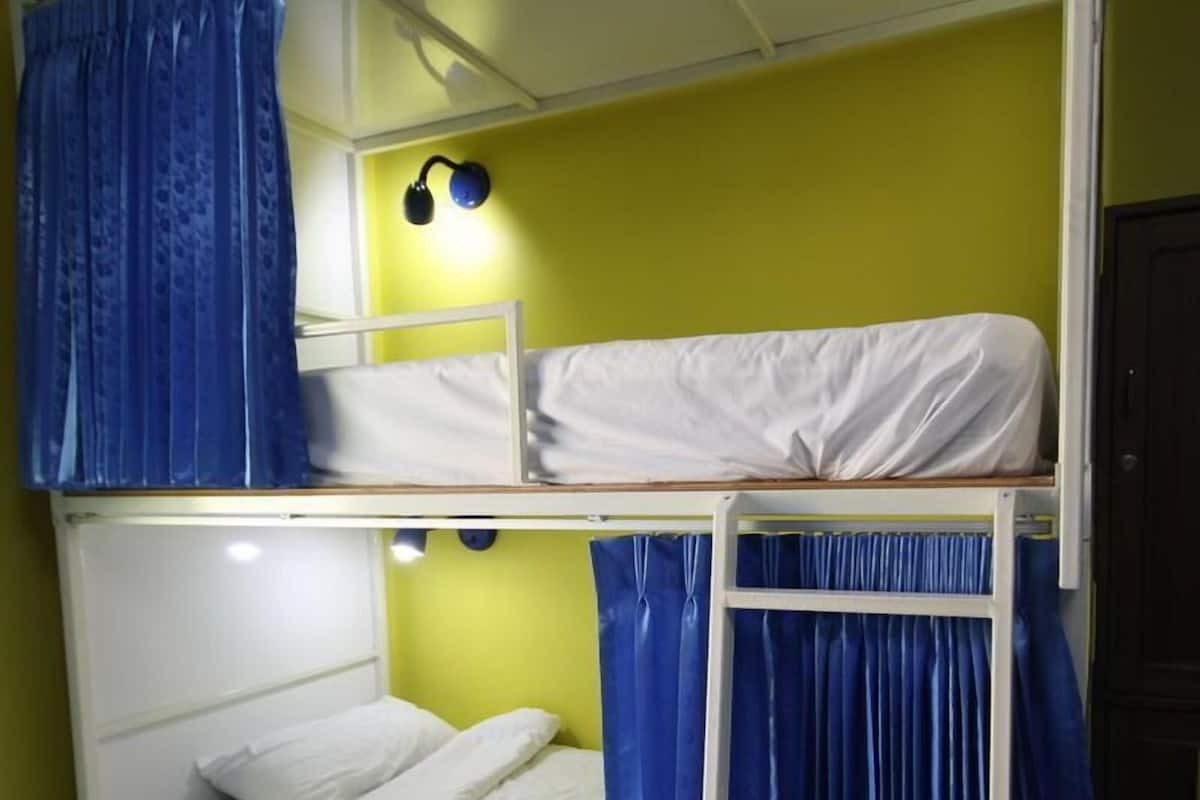 Une chambre avec un lit superposé à deux niveaux, une échelle et une lampe fixée au mur.