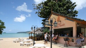 A beachside restaurant with outdoor seating and a view of the sea. - Nomads Chalong Beach, Phuket (Rawai)