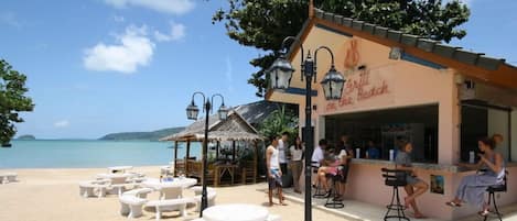 A beachside restaurant with outdoor seating and a view of the sea.