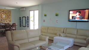 A living room with two beige sofas, a glass coffee table, and a flat-screen TV mounted on the wall. - Nomads Chalong Beach, Phuket (Rawai)