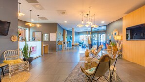 A modern hotel lobby with wicker furniture, a reception desk, and a large window offering a view of the street.