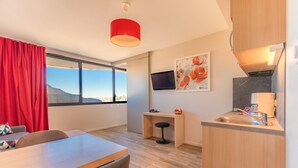 A modern kitchen with a built-in stove, a sink, and a small island. There is a dining area with a table and chairs, and a large window with red curtains.