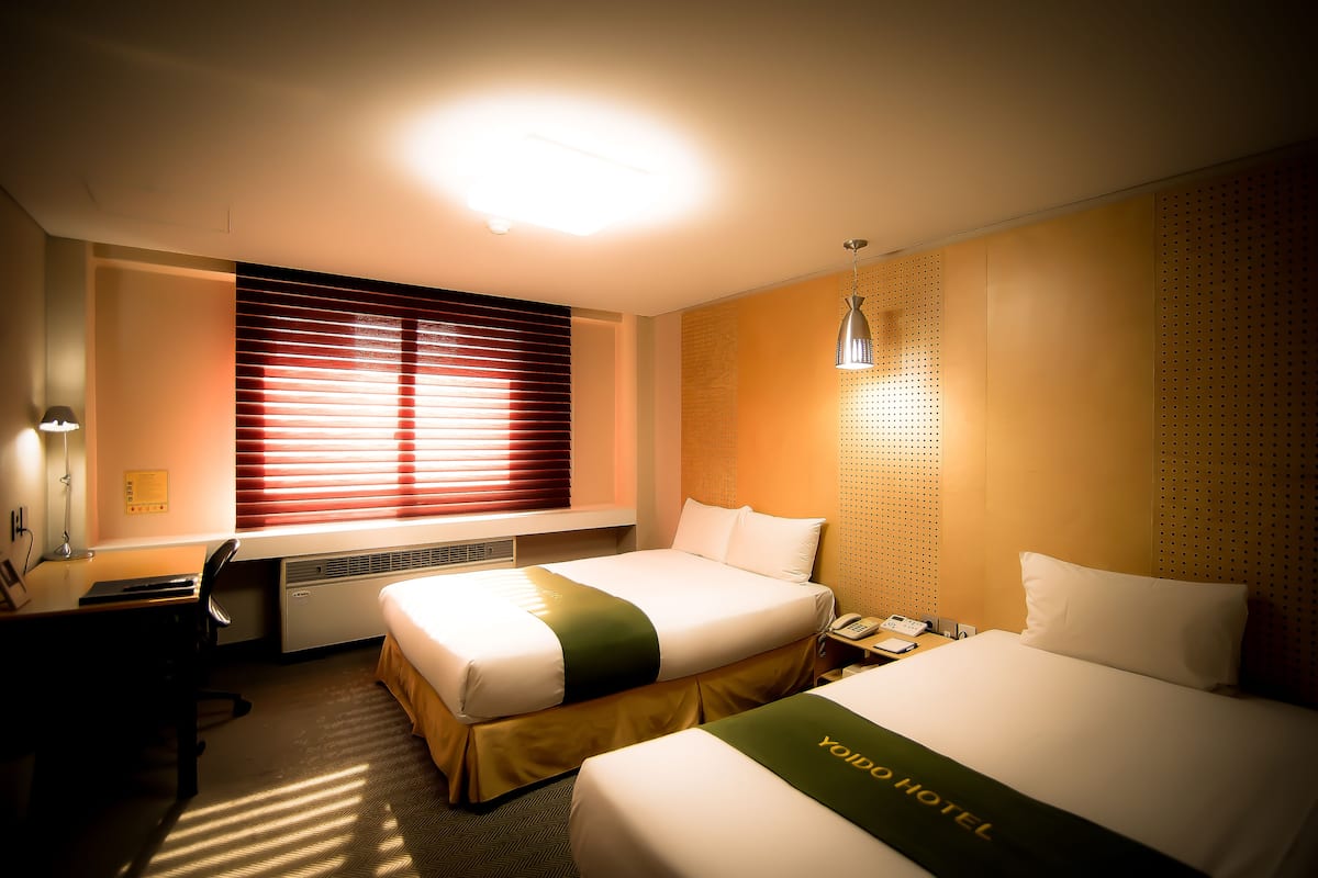 Habitación de hotel con dos camas, un escritorio, una silla, un teléfono y una ventana con persianas.