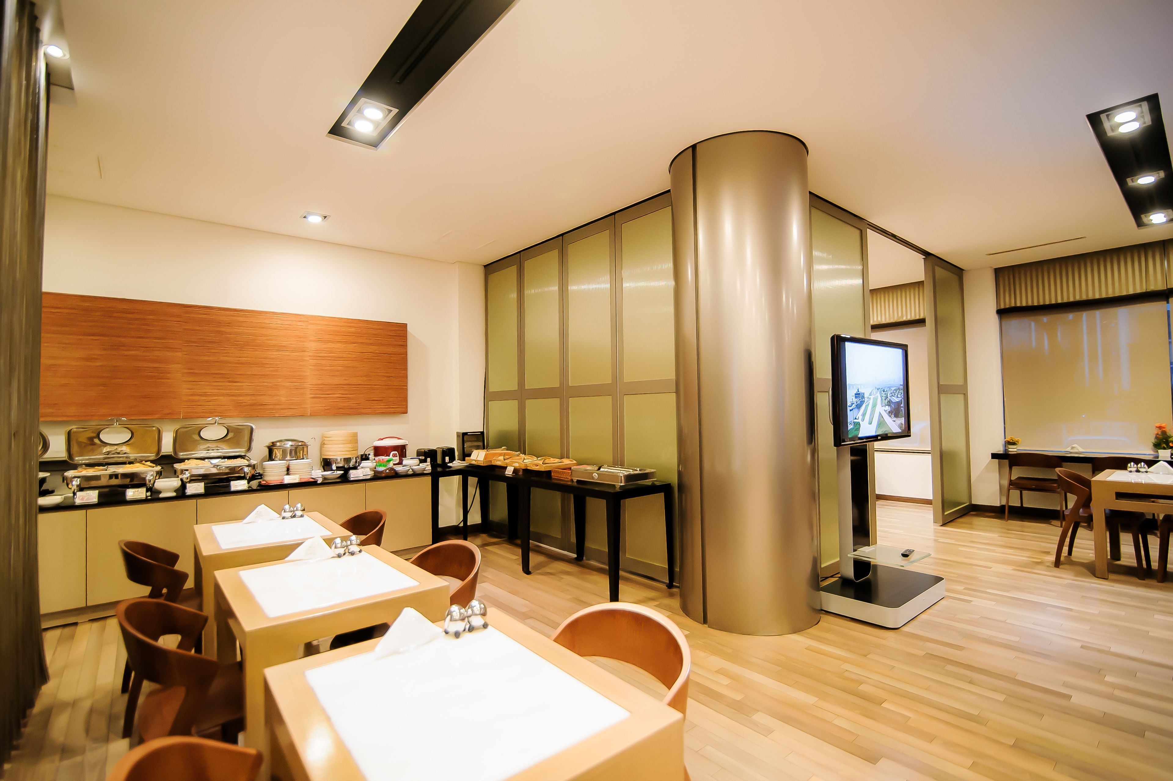 A modern hotel dining area with multiple tables, a buffet, and a television screen.