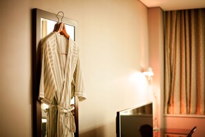 A hotel room with a robe hanging on a wall-mounted rack, a flat-screen TV, and a lamp. - Yoido Hotel (Seoul)