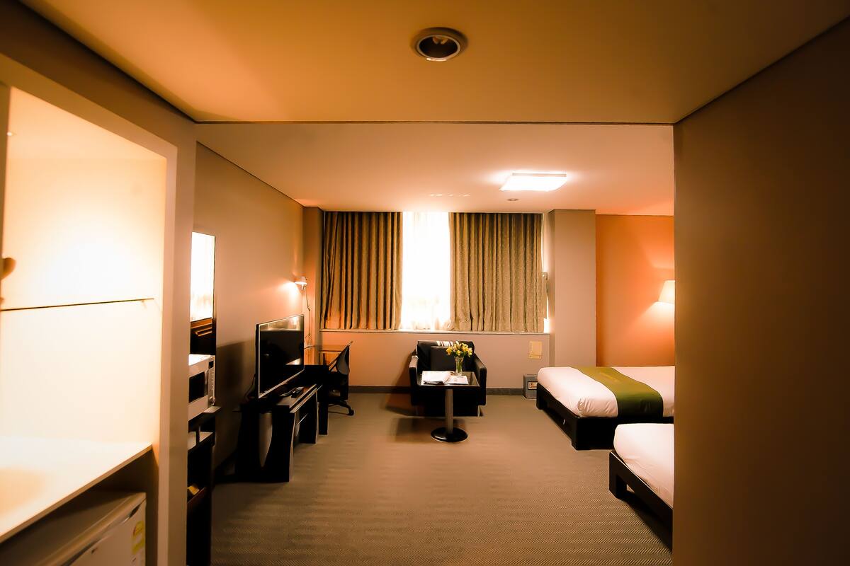 Habitación de hotel con cama, escritorio, silla, televisor y ventana con cortinas.
