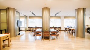 A spacious dining area with multiple tables and chairs, large pillars, and a television on a stand. - Yoido Hotel (Seoul)